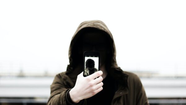 man wearing black hooded jacket and holding smartphone white taking close-up selfie